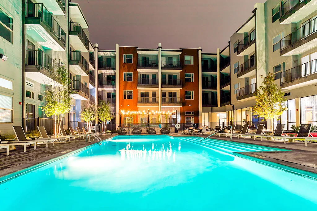 Swimming pool in the middle of the apartment community with several lounge chairs and picnic tables