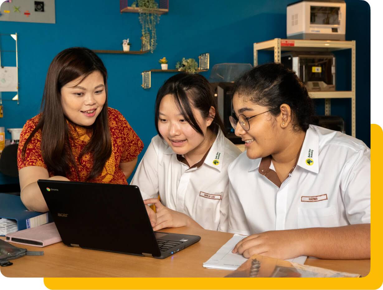 A female teacher and two female students looking at a Chromebook in a classroom.