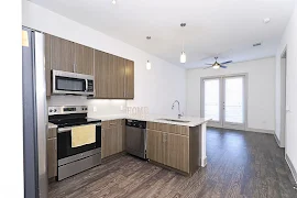 Open kitchen and living room area with wood-inspired flooring, dark cabinets and stainless steel appliances