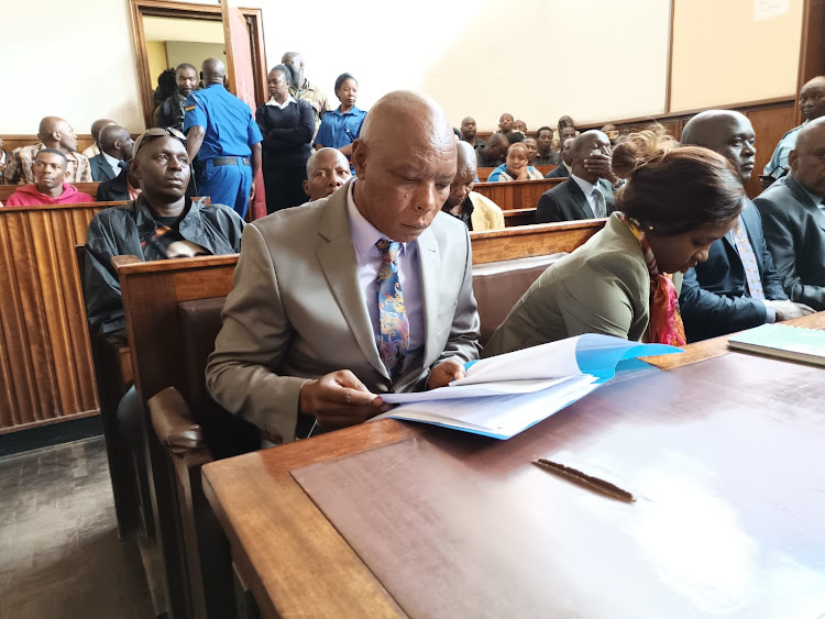 Ex-Mungiki leader, Maina Njenga peruses the file against him at a Nakuru courtroom.