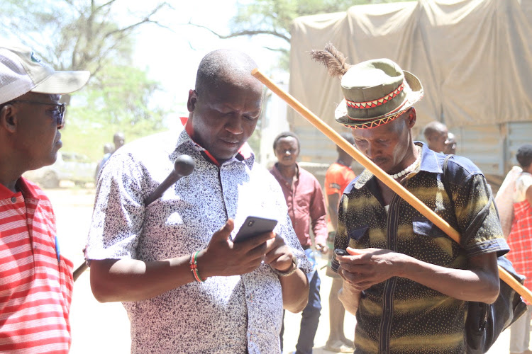 Tiaty MP William Kamket (centre) exchange phone contacts with Pokot residents during relief food distribution in Nginyang, Baringo county, on March 19