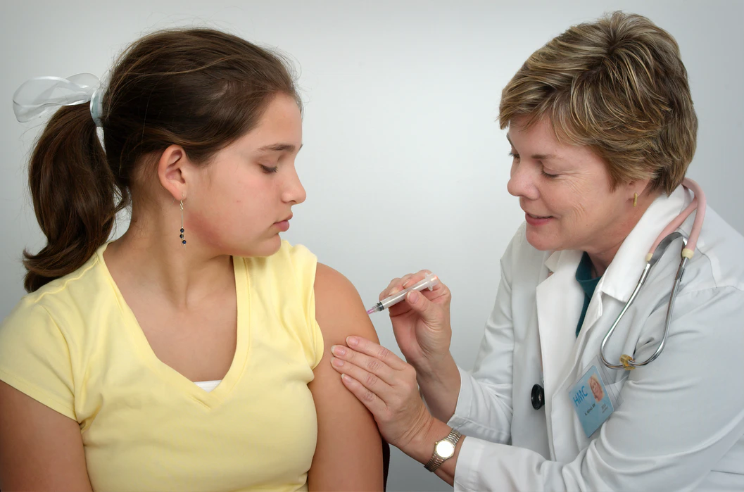 A nurse wearing a white coat injecting a young girl’s arm with a syringe