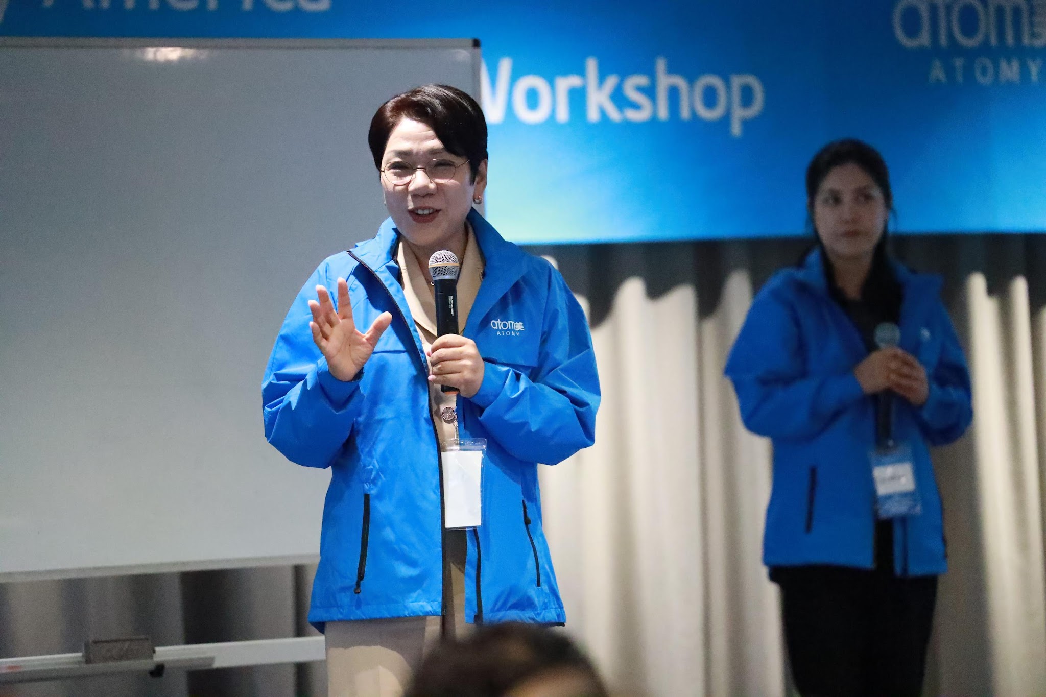 A person in a blue jacket speaking into a microphone

Description automatically generated