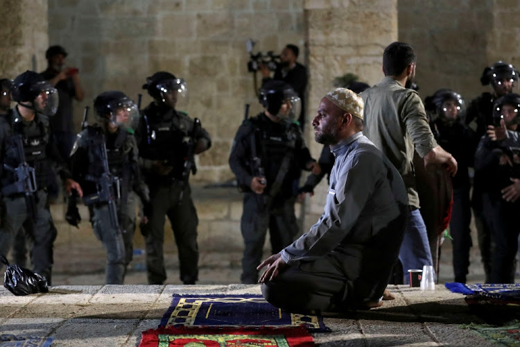 A Palestinian man prays as Israeli police gather during clashes at the compound that houses Al-Aqsa Mosque, known to Muslims as Noble Sanctuary and to Jews as Temple Mount, amid tension over the possible eviction of several Palestinian families from homes on land claimed by Jewish settlers in the Sheikh Jarrah neighbourhood, in Jerusalem's Old City on May 7 2021.