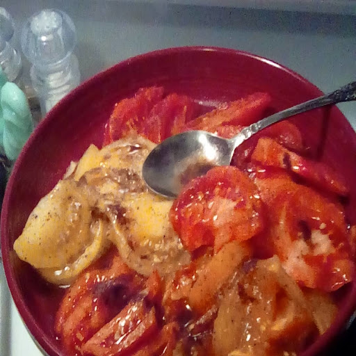 Tomatoes in a red bowl tossed in browned butter with a spoon.