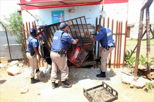 Joburg metro police officers closing a shop after residents looted it on January 22, 2015 in Soweto, South Africa. The looting of shops owned by foreign nationals has spread to other areas in Soweto following an incident where a shop owner shot dead a teenage boy who attempted to rob his shop on Monday.