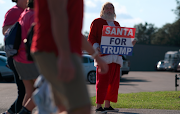 A man dressed as Santa Claus holds a sign as supporters of US President Donald Trump arrive for an election campaign rally at Orlando Sanford International Airport in Sanford, Florida, US on October 12 2020. 
