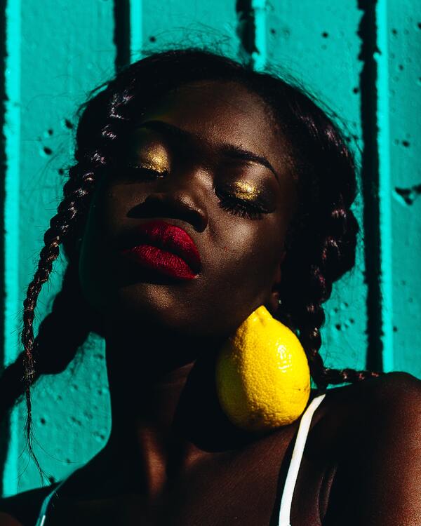 foto de um mulher negra com uma maquiagem dourada com um limão no pescço 