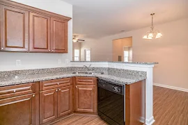 Sink and built in dishwasher in kitchen counters facing connected eat-in bar overlooking living room and patio door ahead