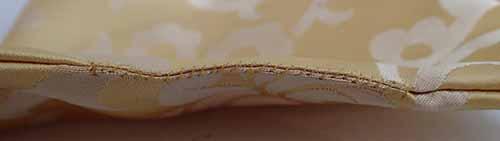 A whip stitch is visible against the cream silk lining, closing the opening to the bottom layer of the bag.