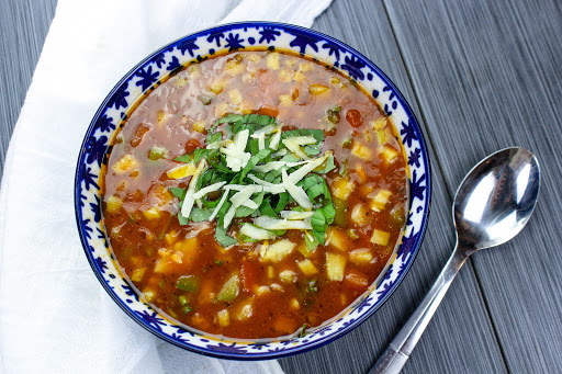 Gazpacho in a bowl with basil and cheese on top.