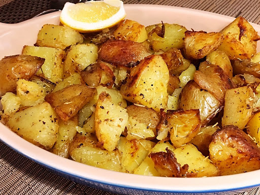 Roasted potatoes in a serving dish garnished with a slice of lemon.