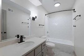 Bathroom with light walls, subway tile tub/shower surround with a curtain rod, tile-inspired floors and dark finishes.