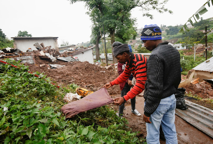 People find clothes of their late relatives in the rubble of a building destroyed by flooding at the KwaNdengezi Station, near Durban, on April 16 2022.