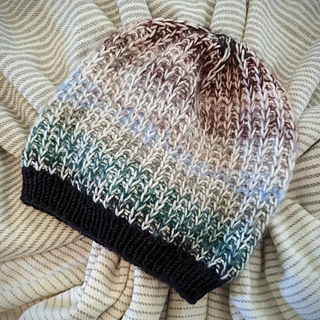 hat knit in color changing yarn on striped fabric background