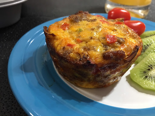 Breakfast muffin served on a blue plate along with kiwifruits and cherry tomatoes.