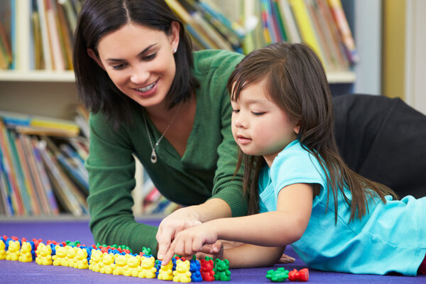 A teacher and child lying on a purple mat with little yellow, blue, red, and green plastic bears lined in rows according to color in front of them.