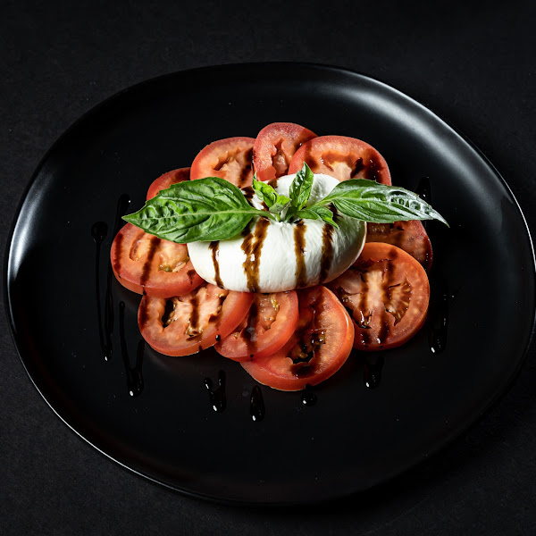 Caprese with burrata cheese and sliced tomatoes topped with balsamic vinegar and fresh basil.