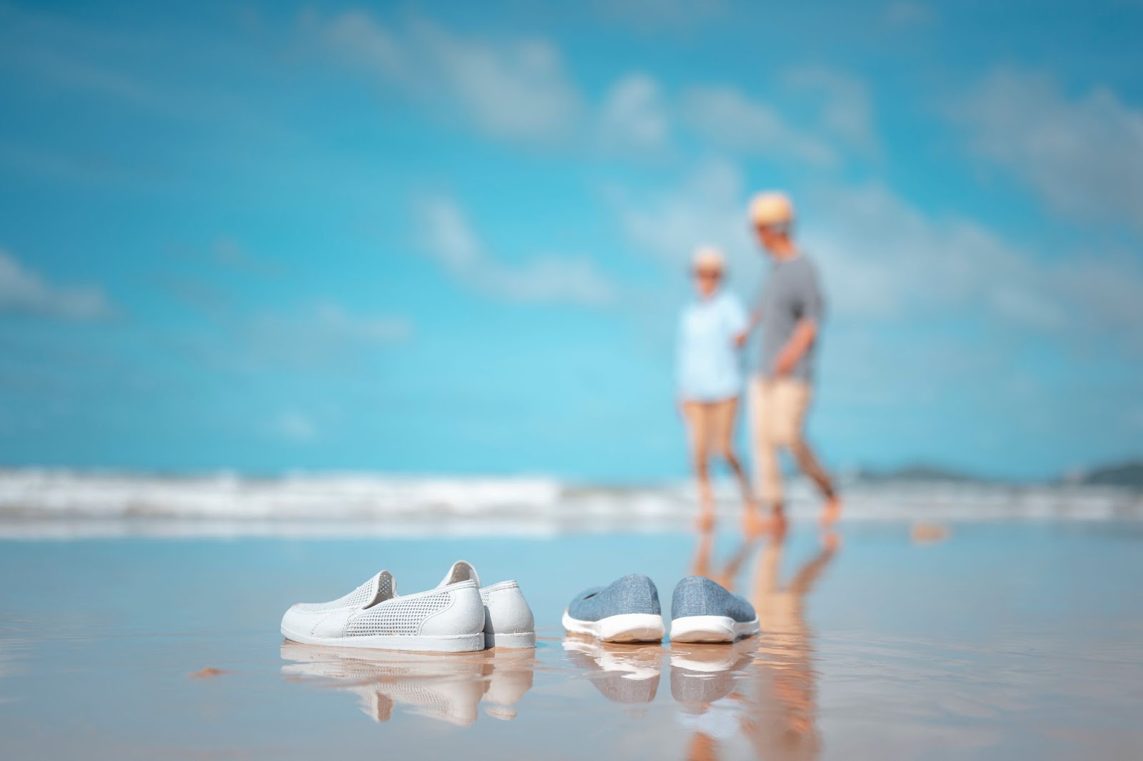 A couple walking hand in hand on a beach with their shoes in the forefront. 