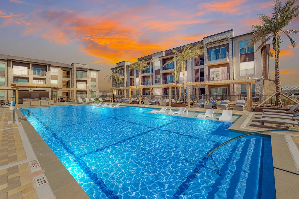 The Haywood's community pool with ledge lounge chairs, large sundeck, pergolas, apartment buildings in background at dusk