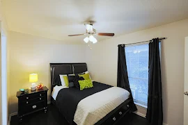 Furnished bedroom with ceiling fan, light walls, and window with blinds