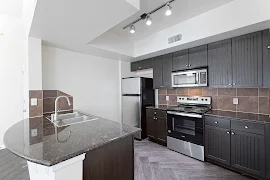 Modern kitchen in an apartment with black and stainless steel appliances, dark cabinets, and a curved breakfast bar.