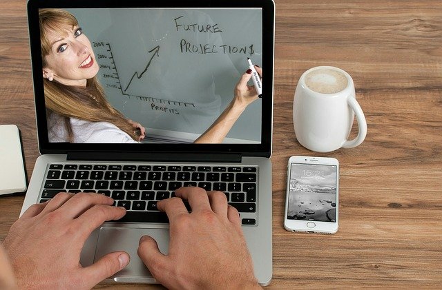 a woman in a white top holding a black marker and teaching on the computer screen. A person taking an online course while drinking a beverage on their silver laptop.
