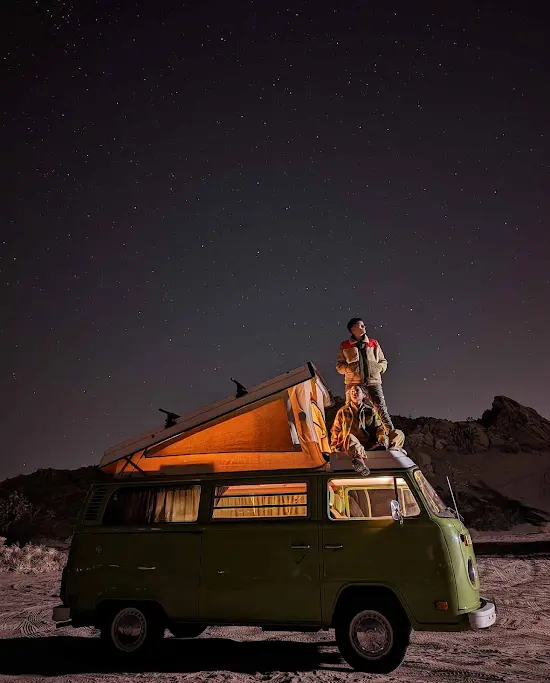 People sitting on top of a van looking up at the stars