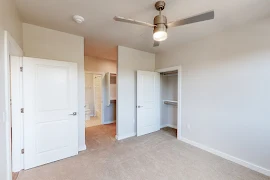 Bedroom with plush carpet, neutral colored walls, ceiling fan, closet area and access to the bathroom