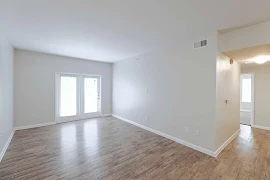 Livingroom with white patio doors with blinds, brown wood flooring and grey walls.