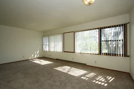 Living room with carpeted flooring, windows, overhead lighting, and white walls with wood trim