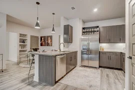 Kitchen with grey wood flooring and canned lighting. Island separates dining area from kitchen with overhead pendant lighting