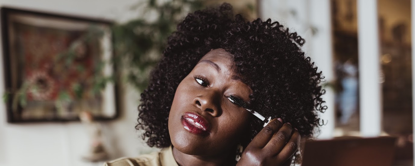 Woman applying mascara to her eyelashes looking side eye to a mirror in her hand