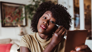 Woman applying mascara to her eyelashes looking side eye to a mirror in her hand