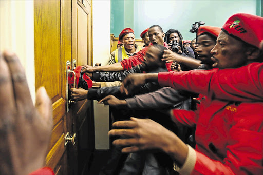 AT THE GATE: Economic Freedom Fighters supporters smash their way into the Gauteng legislature, in the Johannesburg CBD, yesterday after a march to protest against the expulsion of its members for wearing overalls. Police and EFF supporters faced off for hours