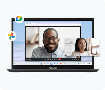 A person sits on a sofa watching a TV presentation. A second person sits on the floor at a coffee table with a Chromebook.