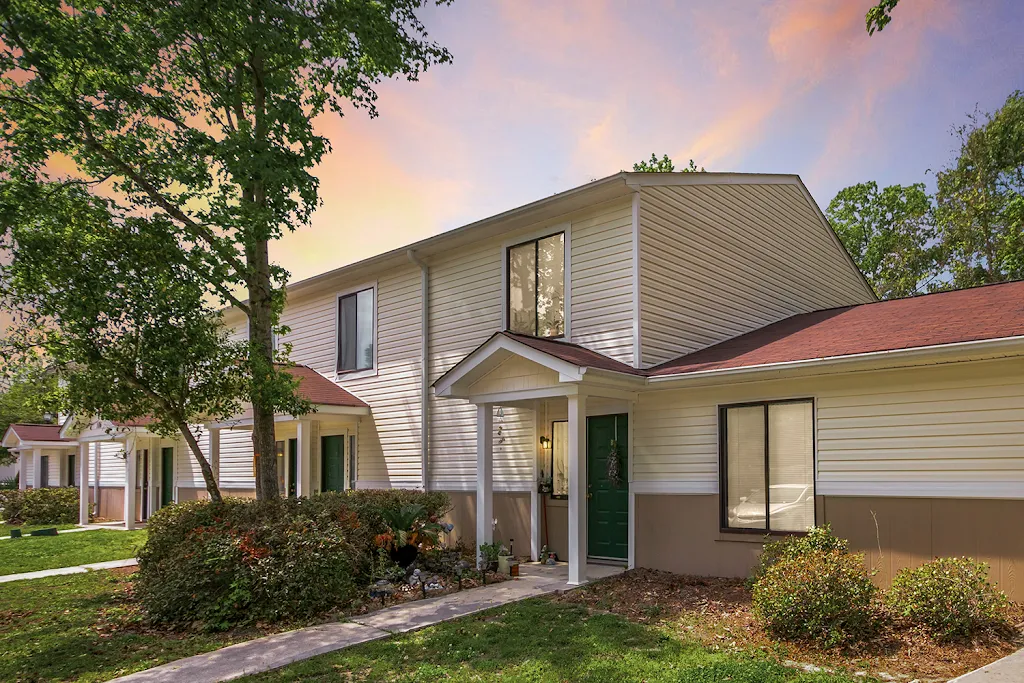 Apartment building with light vinyl siding and red shingles surrounded by grass and simple landscaping