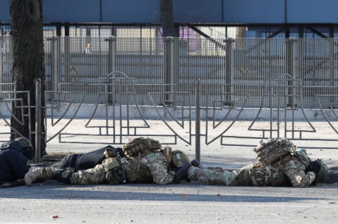 Ukrainian servicemen take cover as an air-raid siren sounds, near an apartment building damaged by recent shelling in Kyiv, Ukraine February 26, 2022