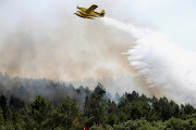 A fire fighting aircraft works to contain a forest fire in Portugal, July 14, 2022. An elderly couple was found dead in burned-out car.