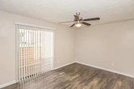 Living area with sliding glass door and vertical blind, wood-inspired floors, neutral walls, white trim, ceiling fan