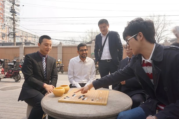 A group of Go players gathered around a board, outside on a cloudy day.