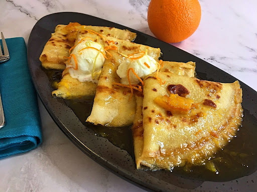 4 crêpes suzette in a beautiful orange liqueur sauce with a couple scoops of homemade vanilla ice cream and garnished with orange zest