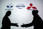 Silhouettes of a man and a woman are seen shaking hands in front of the logos of Renault, Nissan and Mitsubishi.