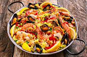  Seafood Spanish paella rice dish with shrimp and mussels shellfish garnished with fresh lemon and served in pan.