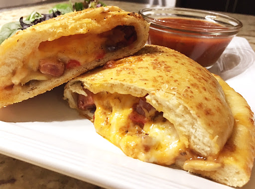 Stuffed calzone on a white plate with a sauce in a small bowl.