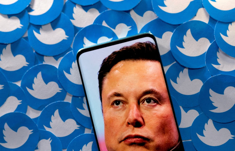 An image of Elon Musk is seen on a smartphone placed on printed Twitter logos in this picture illustration taken April 28, 2022.