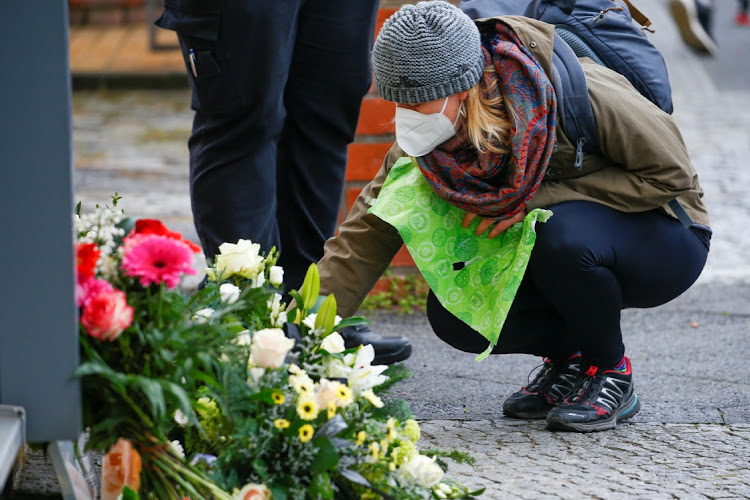 A woman crouches near flowers outside the Oberlin Clinic, where four people were found dead and another seriously injured, following the arrest of a 51-year-old-woman, in Potsdam, Germany, on April 29 2021.