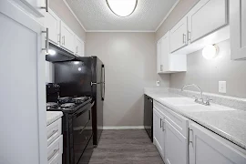 Galley style kitchen with black appliances, white cabinets, light stone inspired countertops, and wood inspired flooring