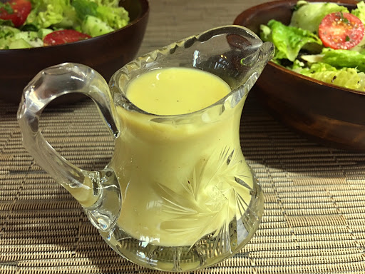 Dressing in a glass jar sitting on a beige table mat with 2 wood bowls of salad in the background.