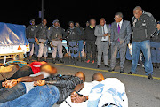 Police Minister Fikile Mbalula is photographed near eight men who the SAPS Western Cape suggested were involved in the violence in Marikana informal settlement in Cape Town.